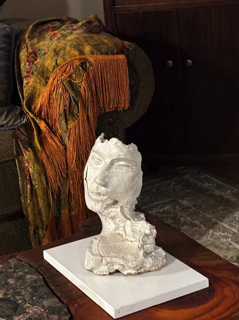 Small white ceramic bust with an open crown sitting on a white board